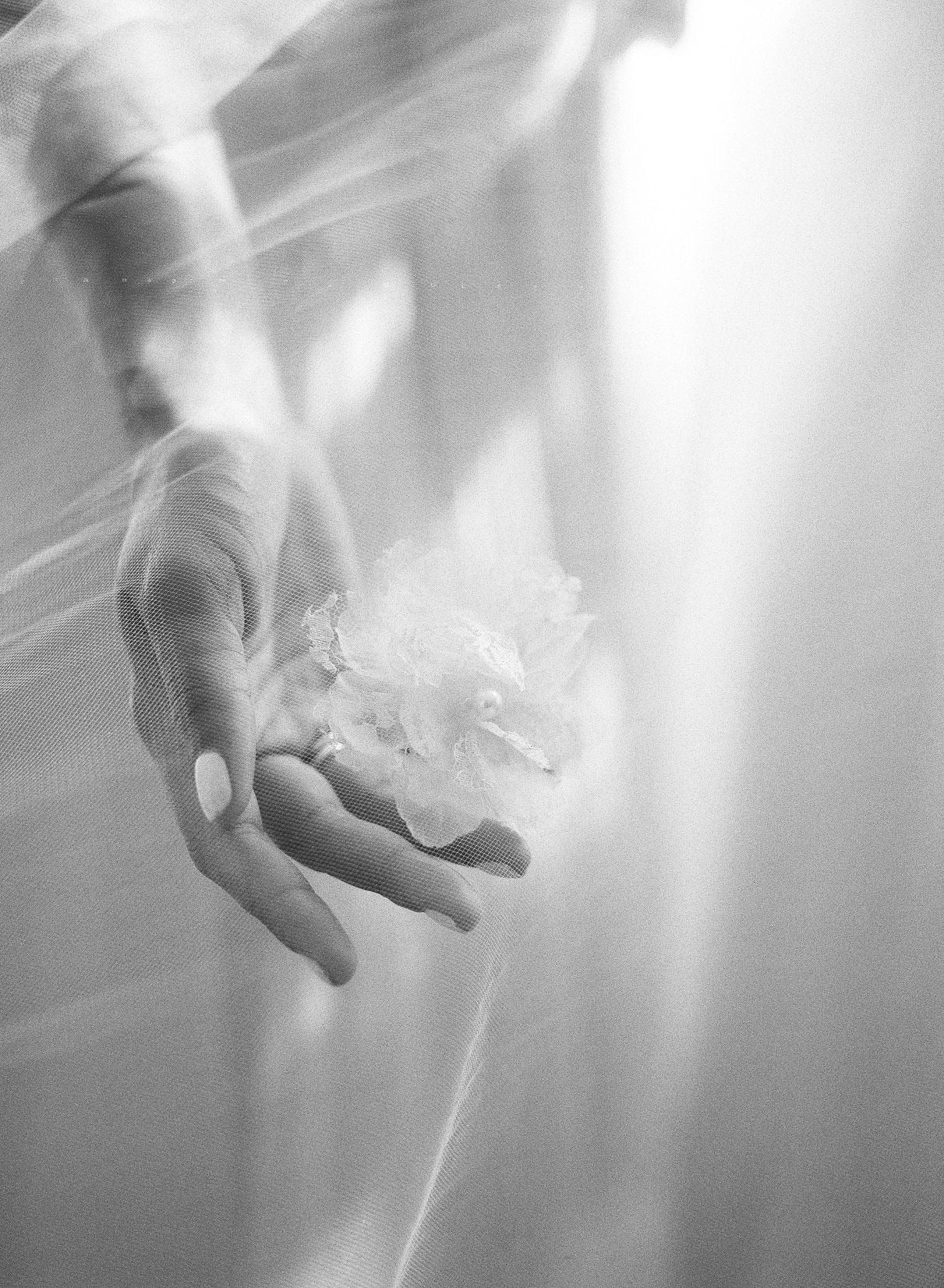 A hand beneath a sheer veil, holding a lace flower